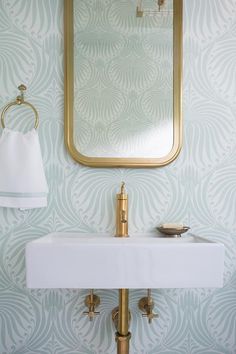 a bathroom sink sitting under a mirror next to a gold faucet and wall paper