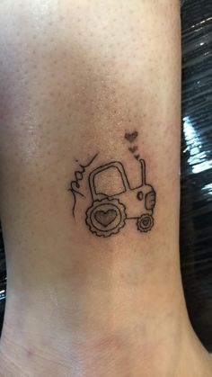 a small tattoo on the ankle of a woman's foot with a tractor and heart