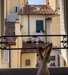 a person's feet are seen through an open window with buildings in the background