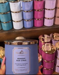 a person holding a candle in front of some shelves with candles on it and other items behind them