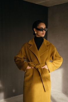 Our mustard gold wrap coat with the loose fit. The H silhouette adds versatility and timeless appeal to your ensemble. With two practical patch pockets, this coat combines convenience and style, allowing you to keep your essentials close at hand. The included belt emphasizes your waist while creating a beautiful and feminine silhouette that accentuates your figure.  Wrap style Loose fit H-silhouette Lowered shoulders line 2 patch pockets Belt Coat fabric: wool 100% Lining fabric: 100% viscose If Luxury Camel Outerwear For Work, Luxury Modern Wool Coat For Fall, Luxury Fall Outerwear For Fashion Statement, Luxury Elegant Camel Wool Coat, Luxury Mustard Winter Outerwear, Timeless Luxury Solid Color Outerwear, Luxury Orange Formal Outerwear, Luxury Wool Coat For Fall, Luxury Midweight Outerwear For Fall