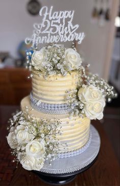 a three tiered cake with white flowers on the top and happy 25th anniversary written in frosting