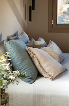 a bed with several pillows on top of it next to a vase filled with flowers