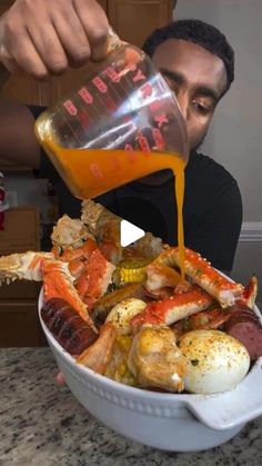 a man pouring orange juice over a bowl of crab legs and corn on the cob