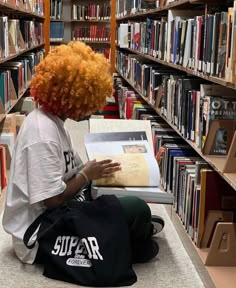 a woman with red hair sitting on the floor in front of bookshelves reading