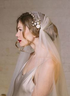 a woman in a wedding dress wearing a veil with flowers on the side and hair comb