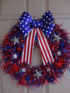 a patriotic wreath with red, white and blue tinsel on the front door is adorned with an american flag bow