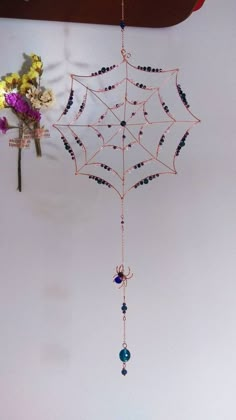 a spider web hanging from the ceiling with beads and flowers on it's side