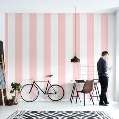 a man standing in front of a pink and white striped wall next to a bike