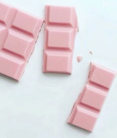 two pieces of pink chocolate sitting next to each other on a white surface with one piece missing