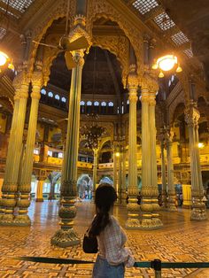 a woman standing in an ornate building looking up at the ceiling and pillars with lights on them