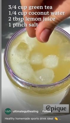 a cup filled with ice sitting on top of a table next to a person's hand