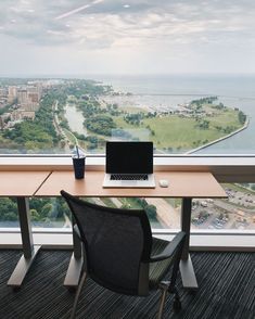 a laptop computer sitting on top of a wooden desk next to a large window overlooking a city