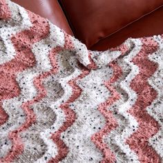 a crocheted blanket sitting on top of a brown leather couch next to a pillow