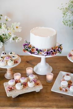 a table topped with cakes and cupcakes on top of wooden trays next to candles