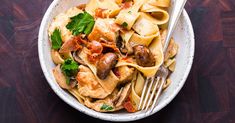 a white bowl filled with pasta and meat on top of a wooden table next to a fork