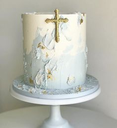 a white cake with gold decorations and a cross on top is sitting on a pedestal