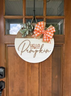 a wooden door with a hello pumpkin sign hanging from it's side and an orange bow on top