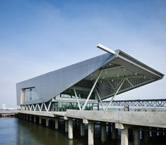 a large metal structure sitting on top of a bridge next to the ocean in front of a building