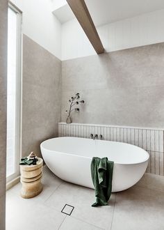 a large white bath tub sitting in a bathroom next to a wooden stool and potted plant