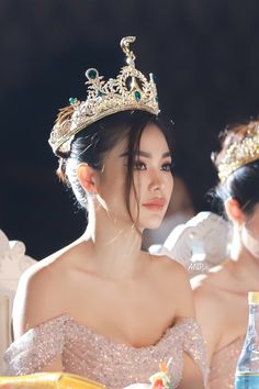 two young women wearing tiaras sitting at a table with drinks in front of them