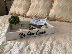 a bed with a tray that says be our guest next to a potted plant