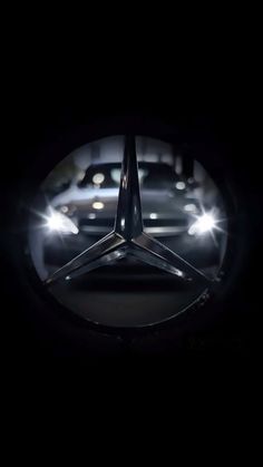 the mercedes logo is shown in front of some cars at night with headlights shining on them