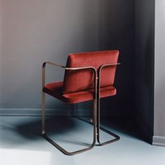 a red chair sitting on top of a white floor next to a gray wall in a room