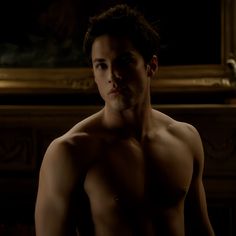 a shirtless young man standing in front of a fire place with his hands on his hips