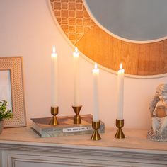 four candles are sitting on top of a mantle next to a statue and a mirror