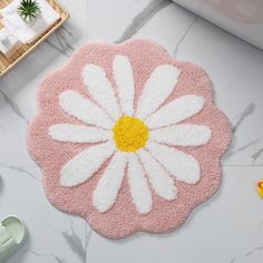 a white and yellow flower on a pink rug next to other bathroom accessories, such as toys