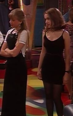 two women standing in front of a tv screen wearing tights and black stockings, one with her hand on her hip