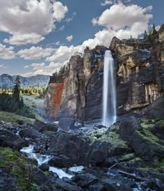 a waterfall in the middle of a rocky mountain range with trees and rocks around it