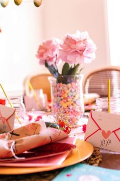 the table is set with pink flowers and candy bar wrappers for valentine's day