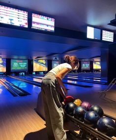 a woman is leaning over to pick up some bowling balls