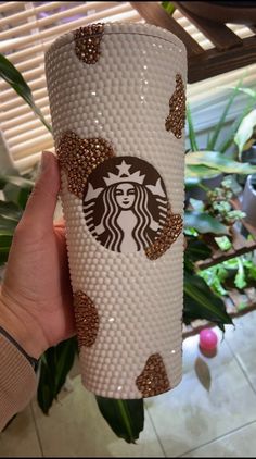 someone holding up a starbucks cup with gold glitters on the bottom, and it's in front of a plant