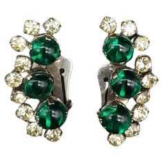 Dimensions: approx. 1.5" x 0.75" each Step back in time with our retro silver-tone clip-on earrings, featuring three cascading emerald crystal cabochons. Each earring is delicately accented with prong-set clear crystals, offering a sparkling contrast that catches the light beautifully. These vintage earrings are the perfect accessory for those who appreciate the elegance of a more stylish era. Add a touch of glamour to your ensemble with these exquisite pieces! Emerald Crystal, Clear Crystals, Step Back, Back In Time, Vintage Earrings, Clear Crystal, Clip On, Prong Setting, In Time