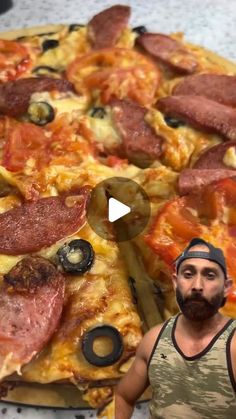 a man standing in front of a pizza with pepperoni and olives on it