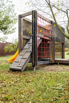 a wooden play structure with a slide in the middle and a yellow slide next to it