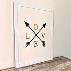 a white framed print with black arrows and the words love in gold foil on it