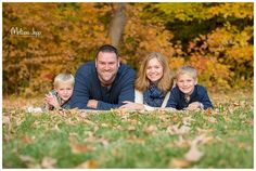 a man, woman and two children laying on the grass in front of some trees