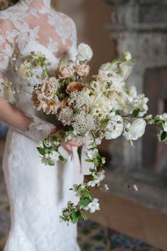 a woman in a wedding dress holding a bouquet of white and pink flowers with greenery