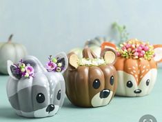 three little ceramic animals sitting on top of a table next to pumpkins and flowers