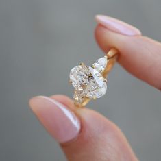 a close up of a person's hand holding a ring with an oval shaped diamond