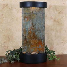 a close up of a water fountain on a table with plants and rocks around it