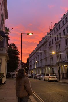 a woman walking down the street in front of some buildings at sunset or sunrise time