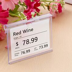 a red wine price label sitting on top of a wooden table next to pink flowers