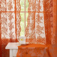 an orange lace curtain with a cup and saucer sitting on a table in front of it