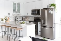 a modern kitchen with stainless steel appliances and white counter tops, along with stools