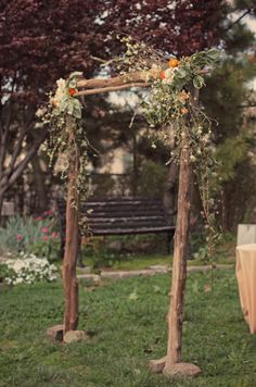 an outdoor wedding ceremony setup with flowers and greenery on the arbor, in front of a wooden bench